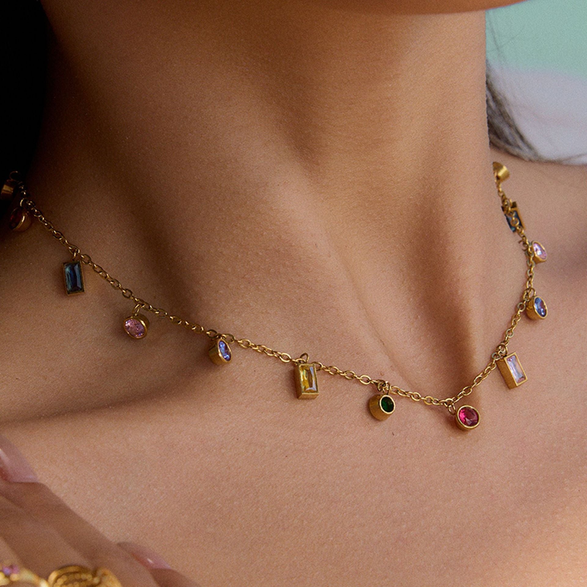 Close-up of woman wearing rainbow crystal charm necklace, layered on collarbone under sunlight