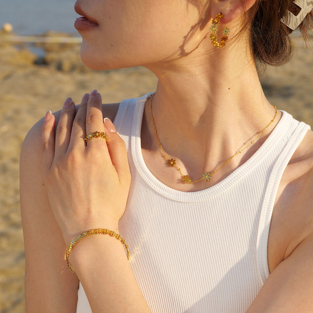 woman wearing daisy hoop earrings, matching floral necklace, ring and bracelet in sunny outdoor beach setting