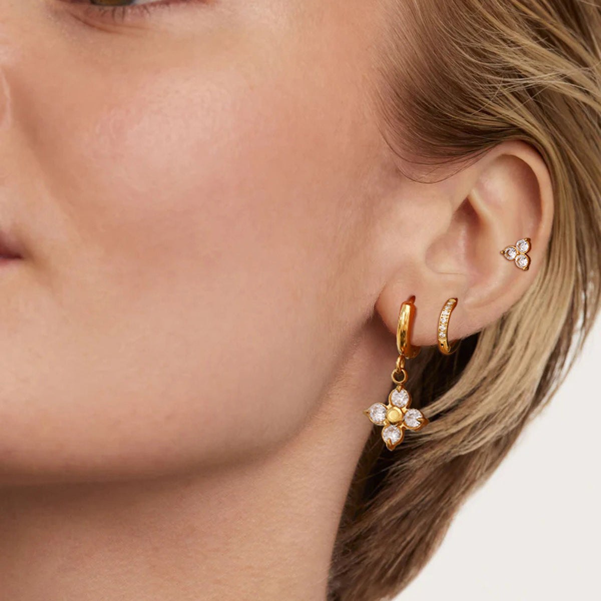 Woman wearing layered gold earrings with dangling flower charm and small zircon hoops