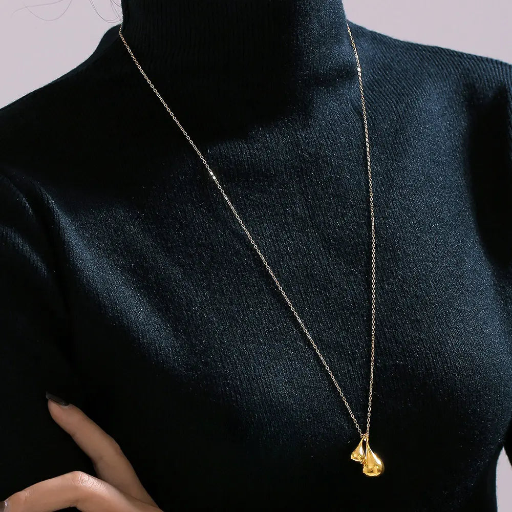 Model wearing a golden titanium plated water droplet pendant necklace, styled with a black turtleneck