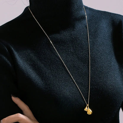 Model wearing a golden titanium plated water droplet pendant necklace, styled with a black turtleneck
