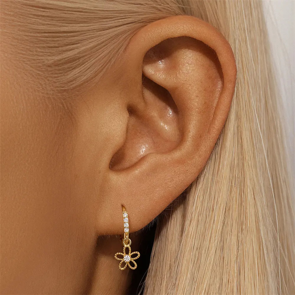 Close-up view of gold flower charm hoop earrings on the ear, showcasing their delicate design and shimmering details.