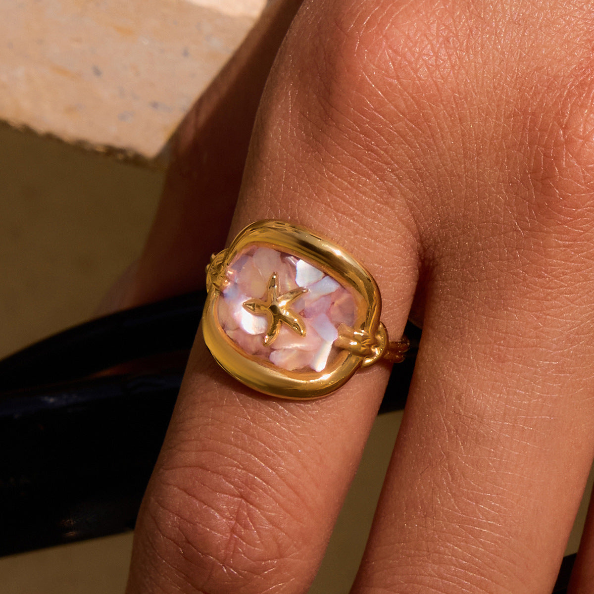 Woman wearing pink seashell ring under sunlight, close-up on finger