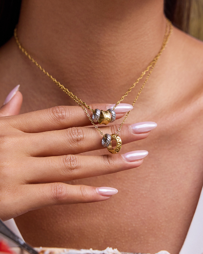 Gold necklace with a pendant held by a hand against a neutral background