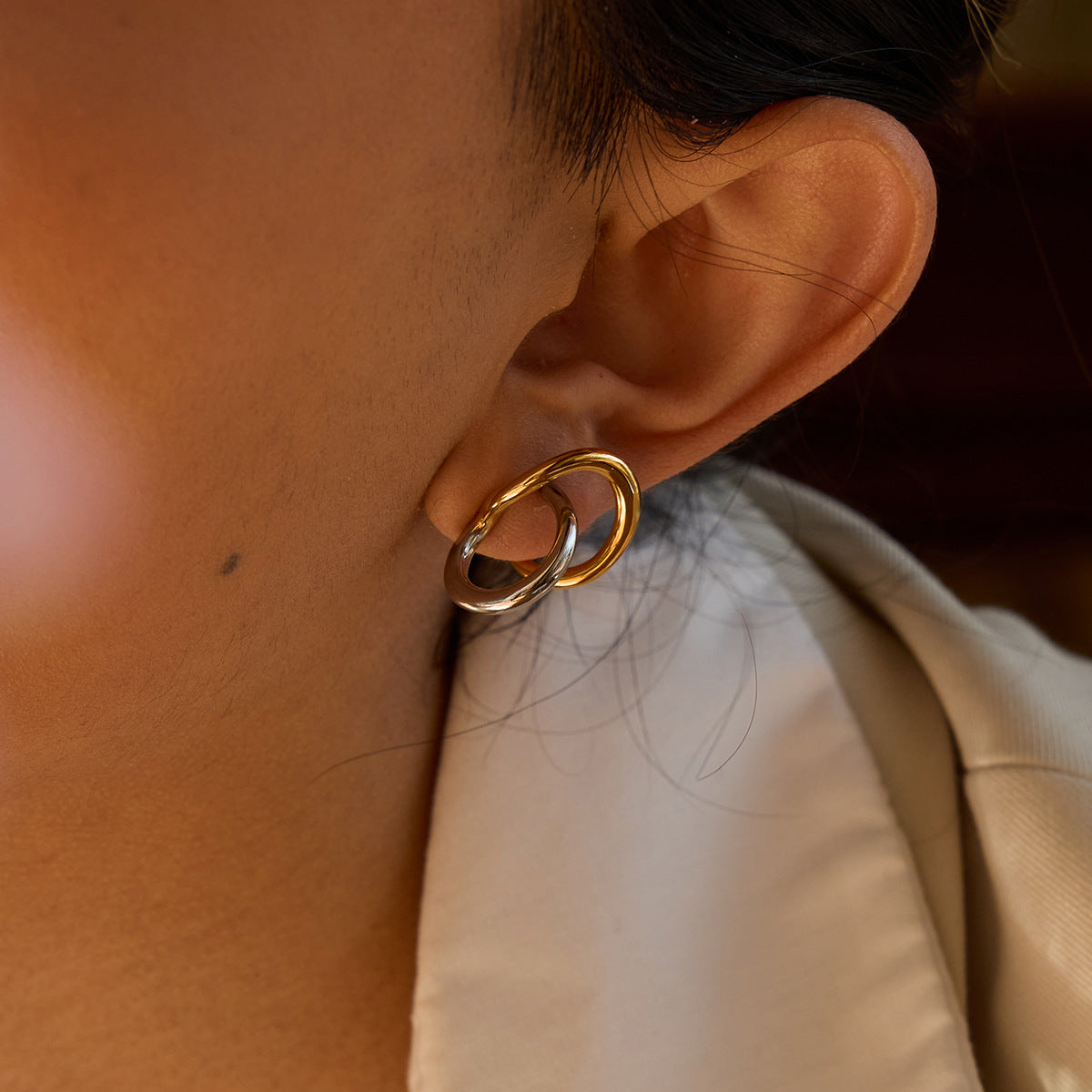 Close-up of gold and silver double hoop stud earring on model's ear, modern fashion jewelry