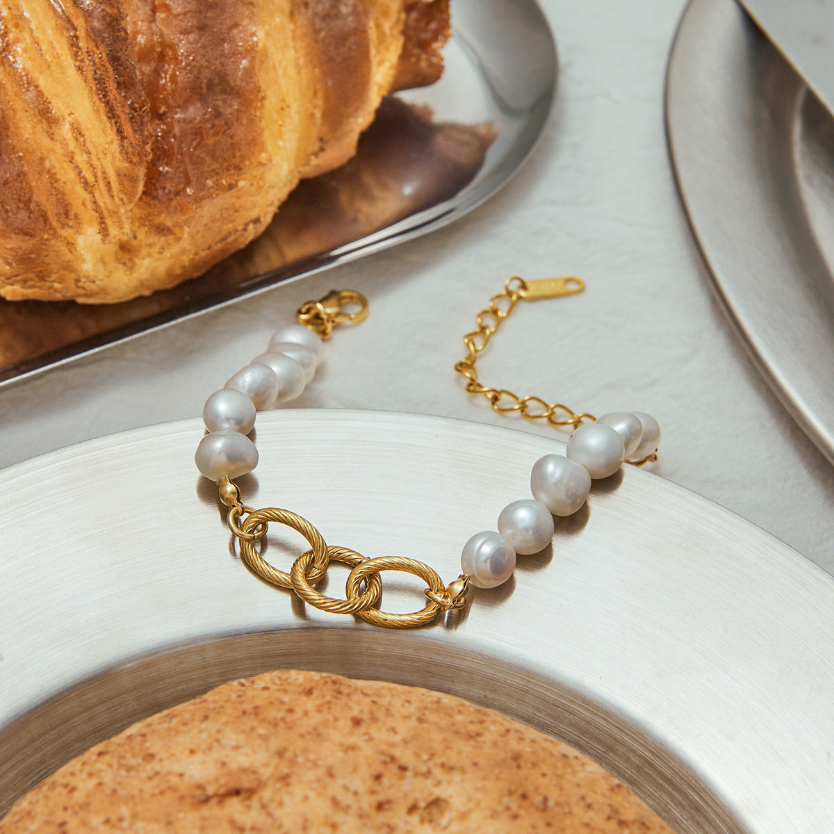 Gold link bracelet with natural pearls on a plate with rustic bread
