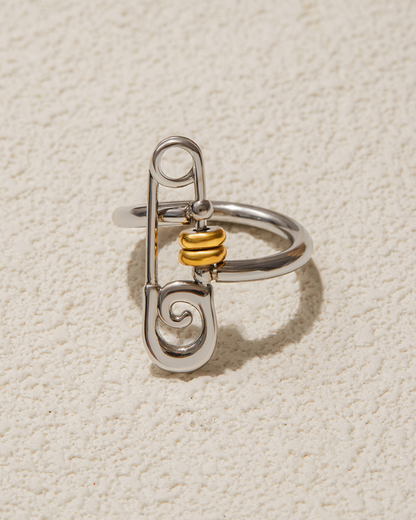 Silver safety pin-shaped ring with gold center on a beige textured background