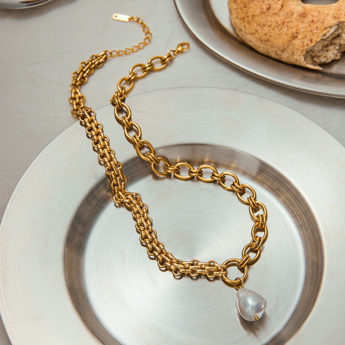 Fashion-forward gold pearl necklace displayed on silver plate with bakery aesthetic