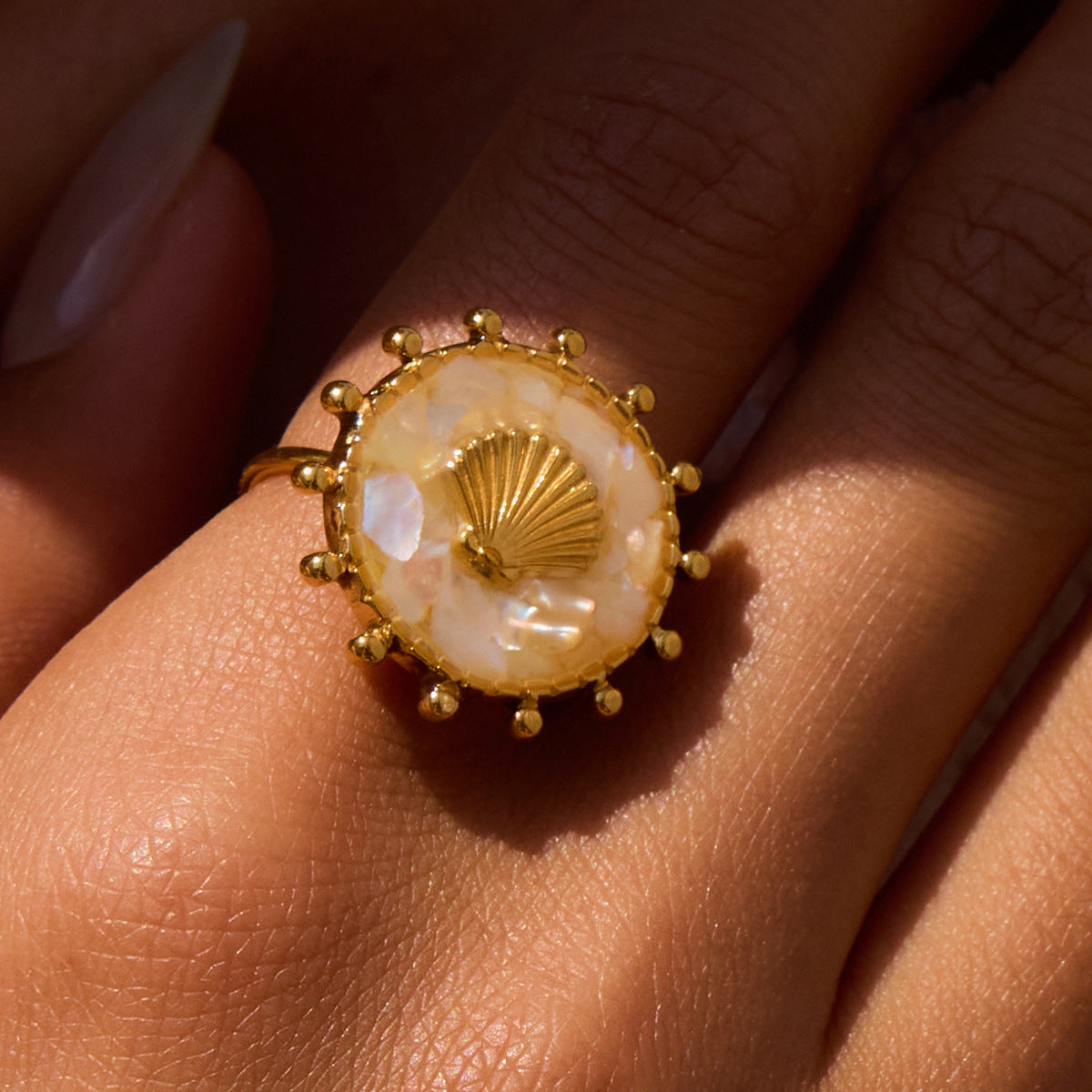  Model hand wearing iridescent white resin shell ring, layered with gold jewelry