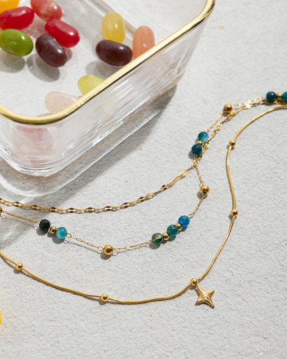 Gold necklaces with beads on a light gray surface with jelly beans in the background