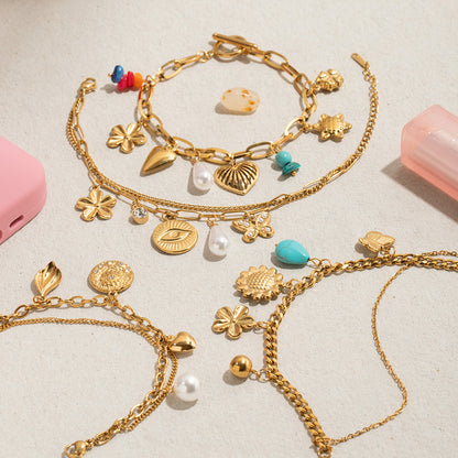 Flat lay of multiple gold charm bracelets with pearls, eyes, hearts and enamel pieces
