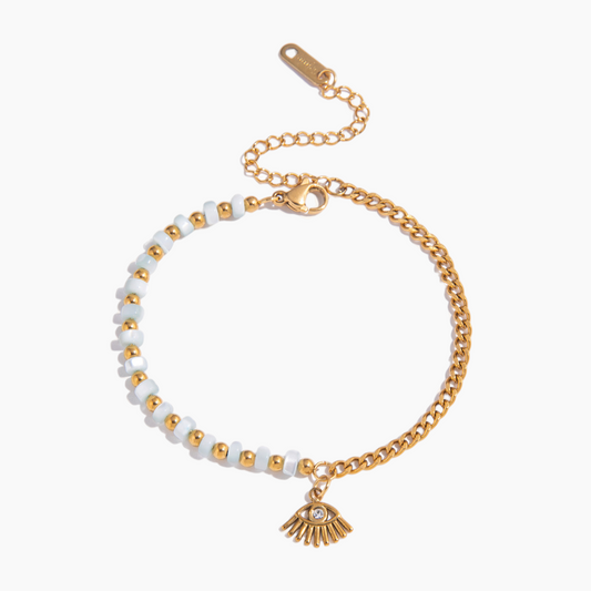 Gold and white beaded bracelet with a small charm on a white background