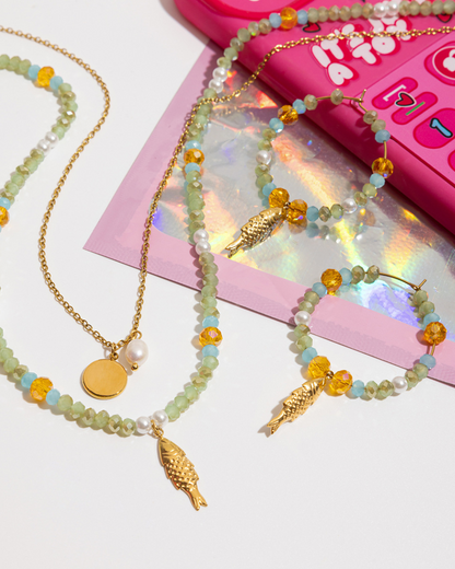 Beaded necklaces with gold fish pendants on a pink toy phone background