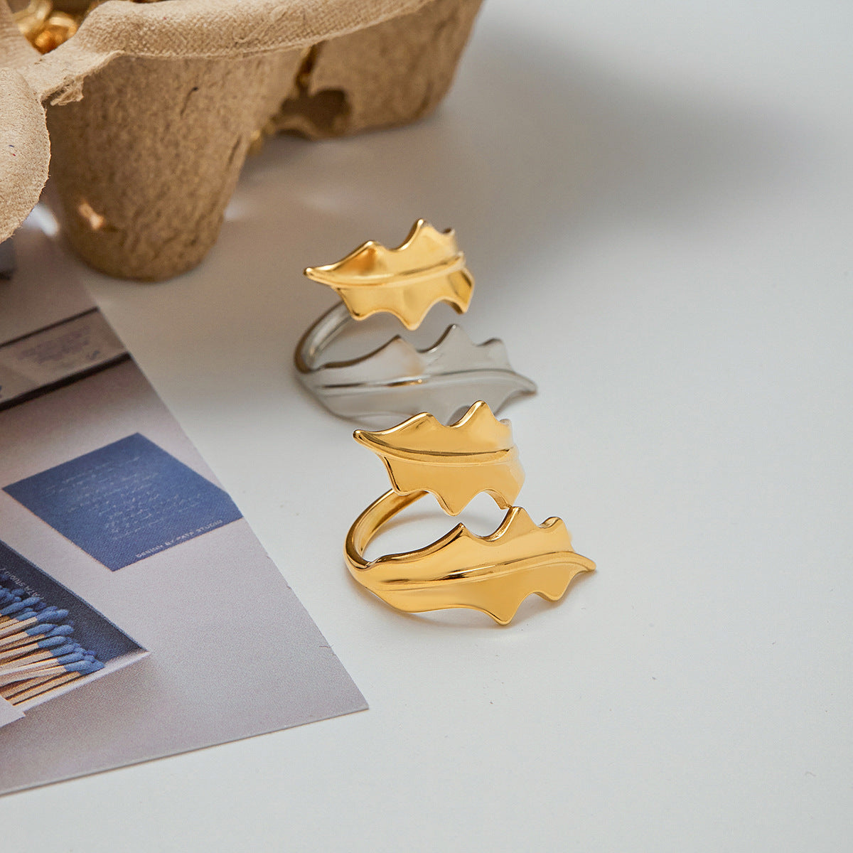 Statement leaf wrap ring in gold and silver finish resting on white surface