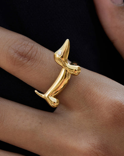 Gold dog-shaped ring on a person's finger against a black background