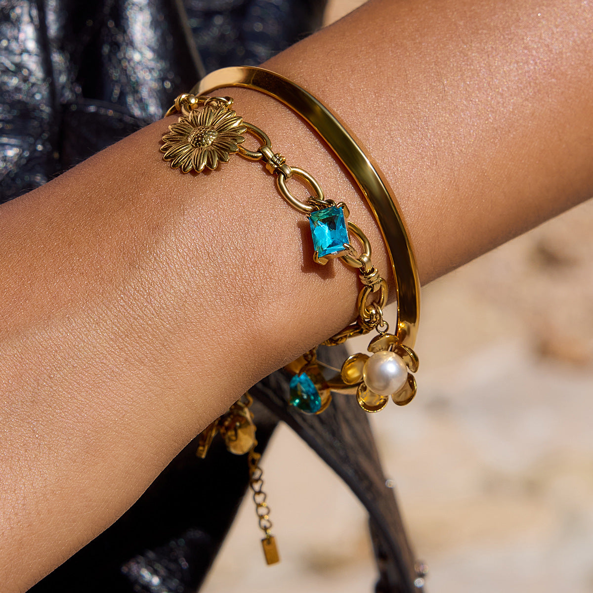 Model wearing gold charm bracelet with ocean blue stones and pearl flower
