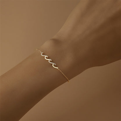 Gold wave design bracelet shown on arm with soft background