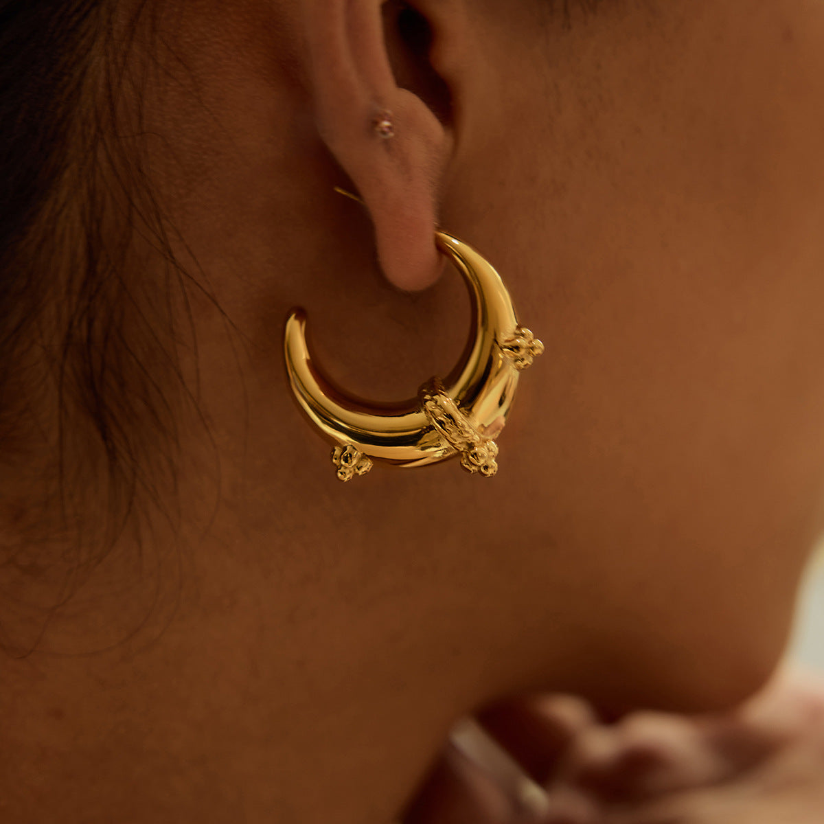 Close-up of curved gold earrings on ear, paired with casual bun hairstyle