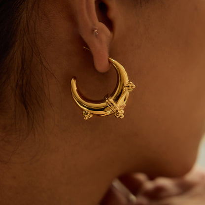 Close-up of curved gold earrings on ear, paired with casual bun hairstyle