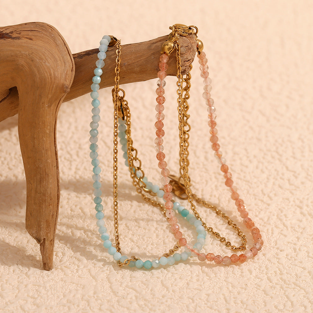 Set of blue and coral bracelets with glass beads and golden chains styled on driftwood.