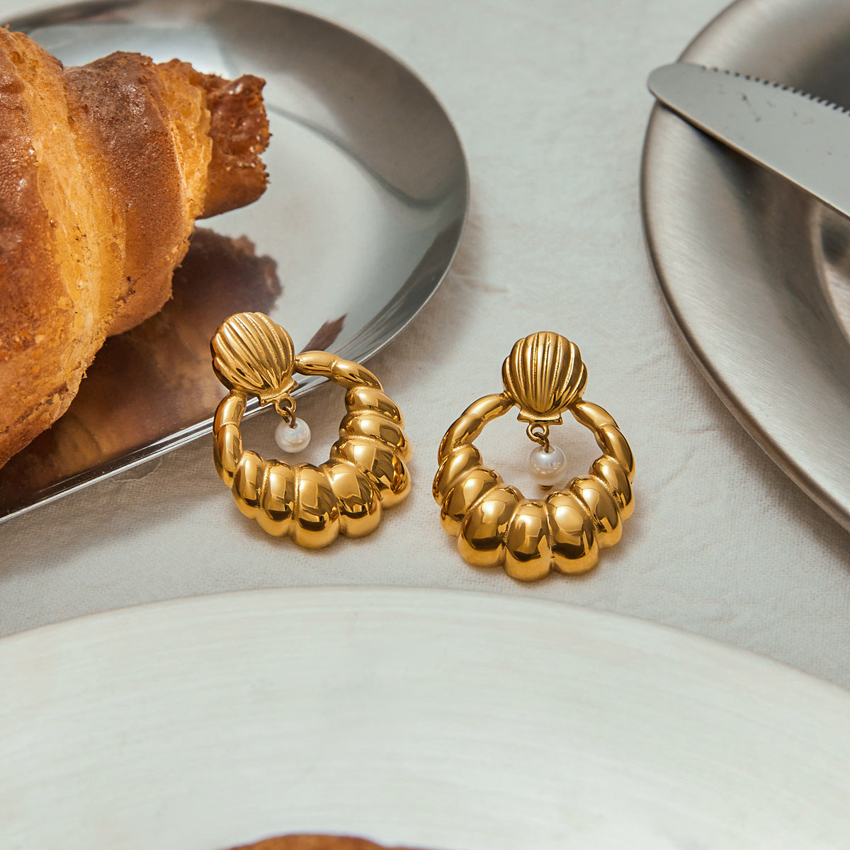 Gold seashell hoop earrings with dangling pearl on white background