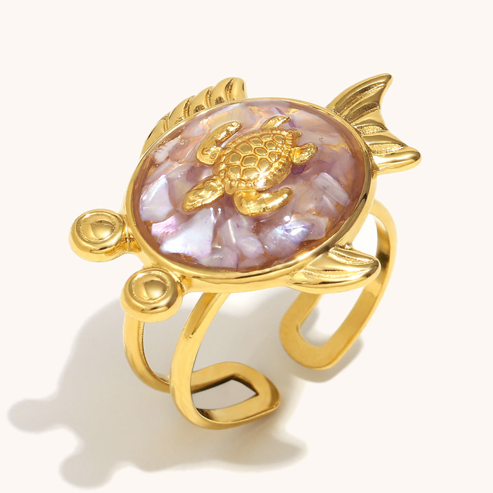 Gold turtle ring with purple shell mosaic design on seashell backdrop