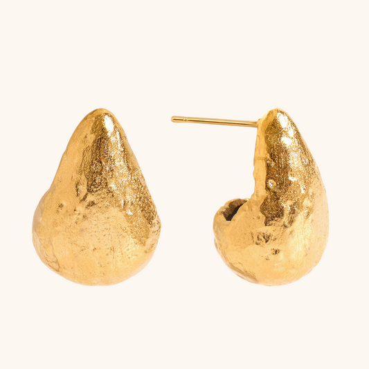 Close-up of gold teardrop earrings on textured stone background