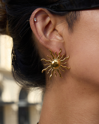 Gold sun-shaped earring worn by a person with a blurred background
