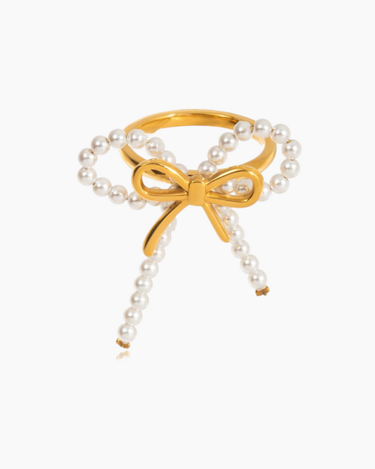 Gold bow-shaped ring with pearl details on a white background