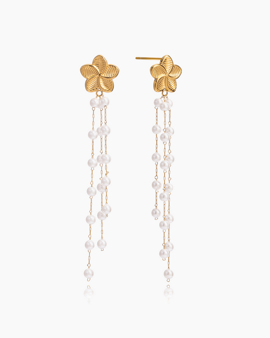 Gold earrings with floral tops and pearl chains on a white background