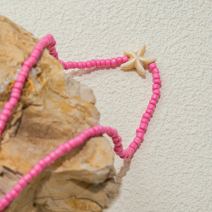 Pink starfish necklace styled on a tray next to beach-themed decor, showing waterproof and non-fade quality.