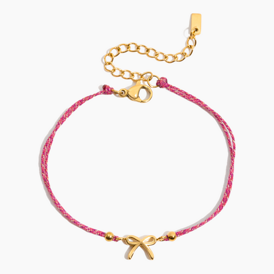 Pink bracelet with gold bow charm on a white background