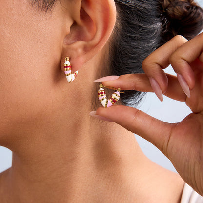 Woman wearing one heart-shaped hoop earring while holding the second one with manicured fingers