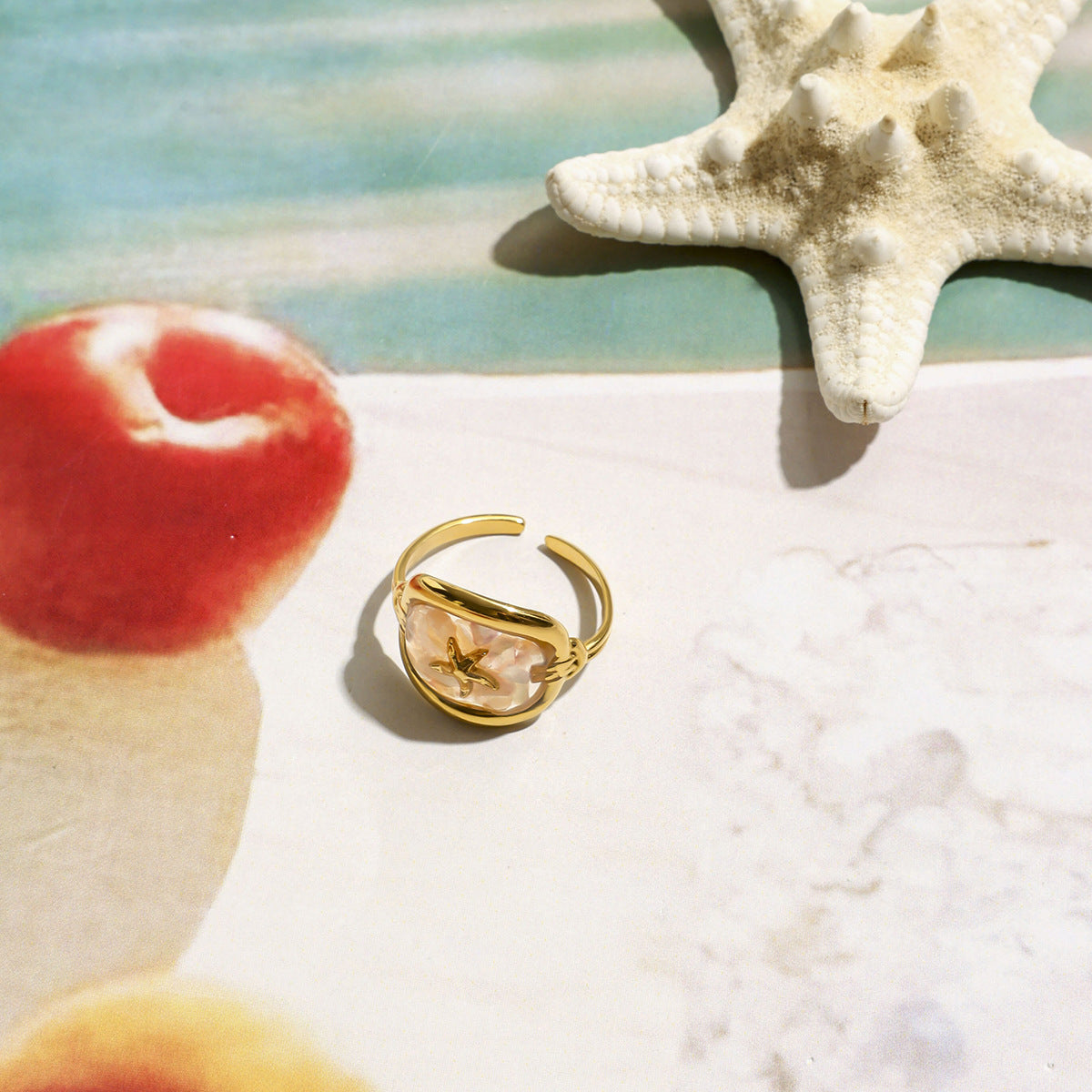 Gold starfish ring styled on a beach-themed background with sea elements