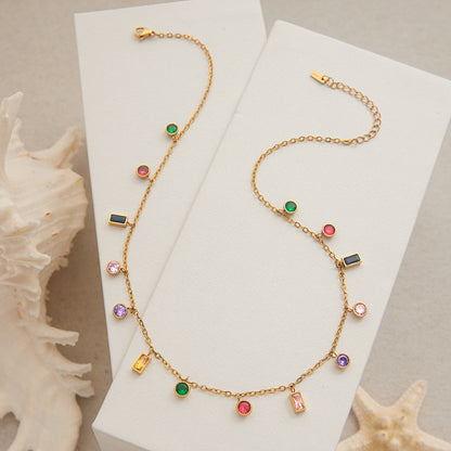 Gold chain necklace with rainbow gemstones styled on beige linen with seashells, beach theme