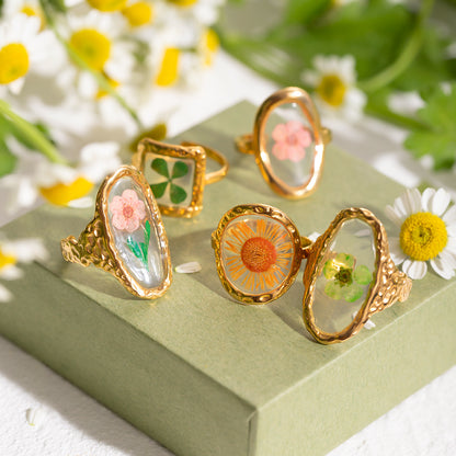 Group of flower-themed resin rings on floral box, sunlight filtering over petals
