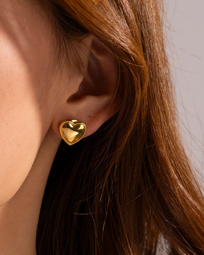 Gold heart-shaped earring worn by a person with brown hair.