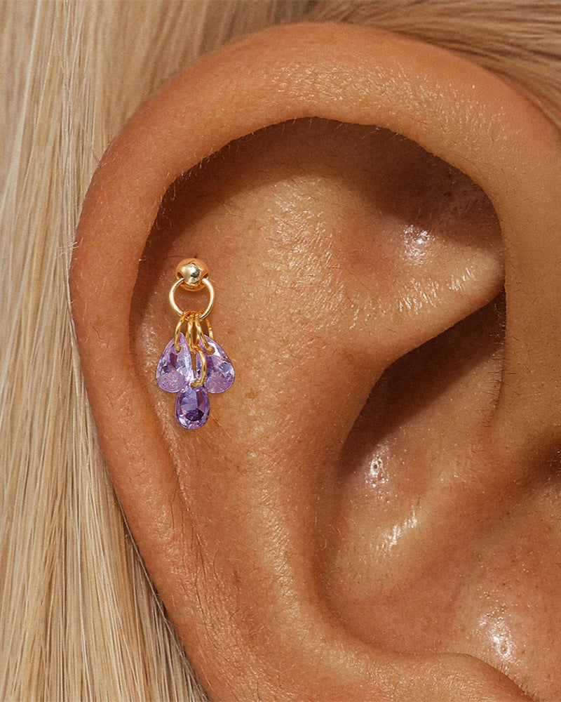 Gold earring with purple gemstones worn in an ear
