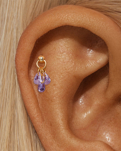 Gold earring with purple gemstones worn in an ear