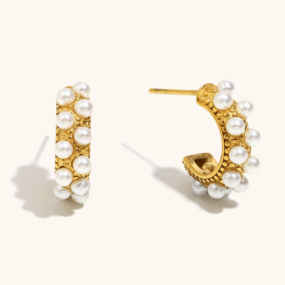 Close-up of textured pearl-studded gold hoop earrings on light background