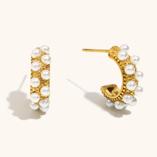 Close-up of textured pearl-studded gold hoop earrings on light background