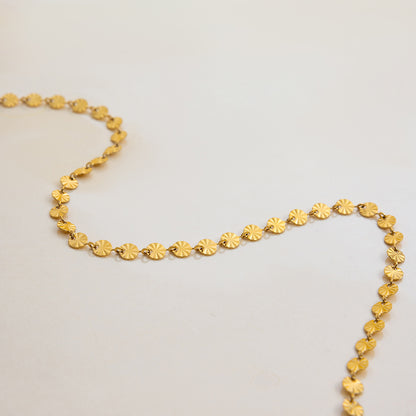 Close-up of gold round disc necklace shining under direct beach sunlight