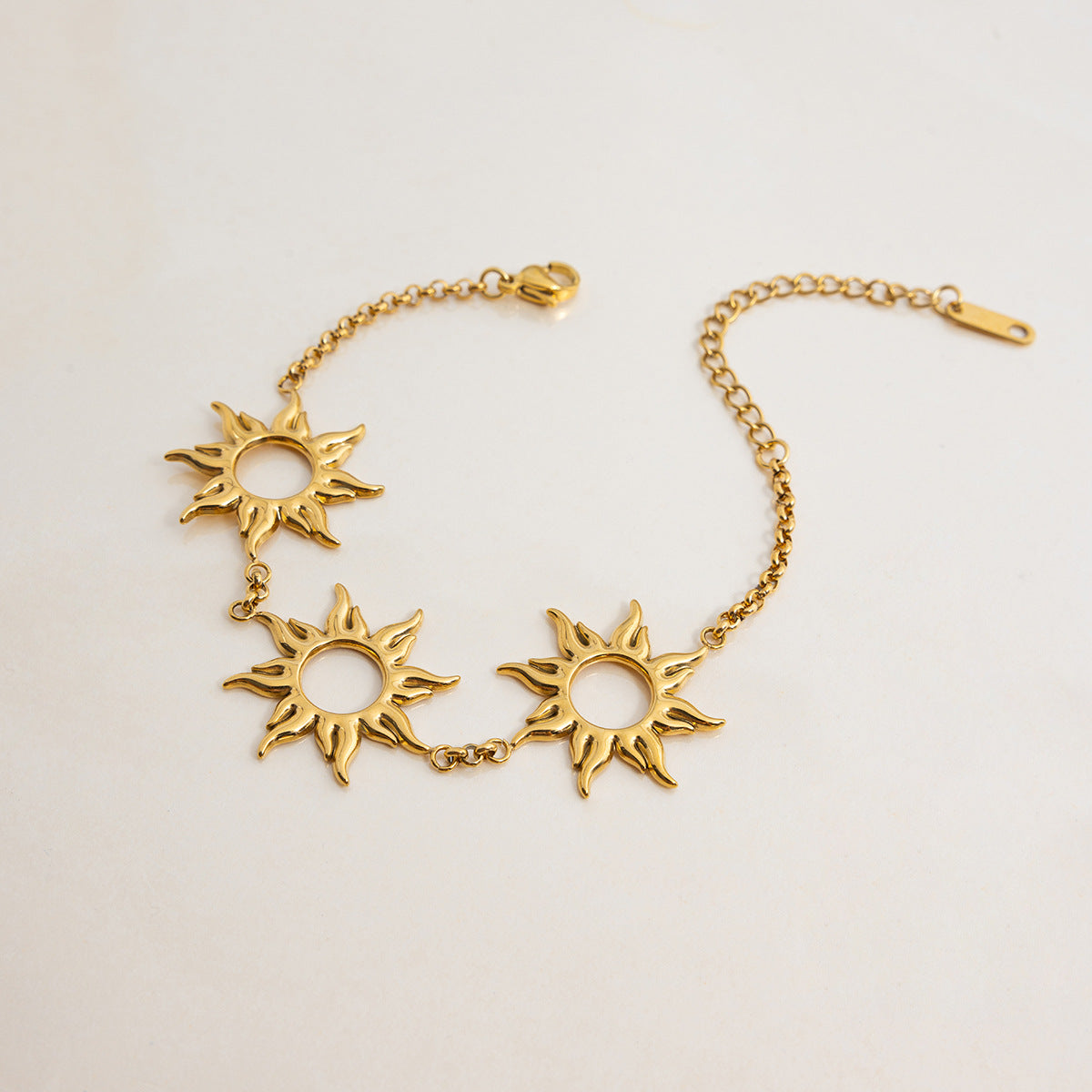 Studio shot of gold bracelet with three sun-shaped pendants on cream background