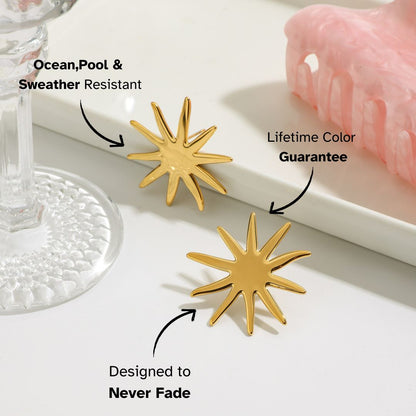 Gold sunburst stud earrings styled next to clear glass and pastel accessories