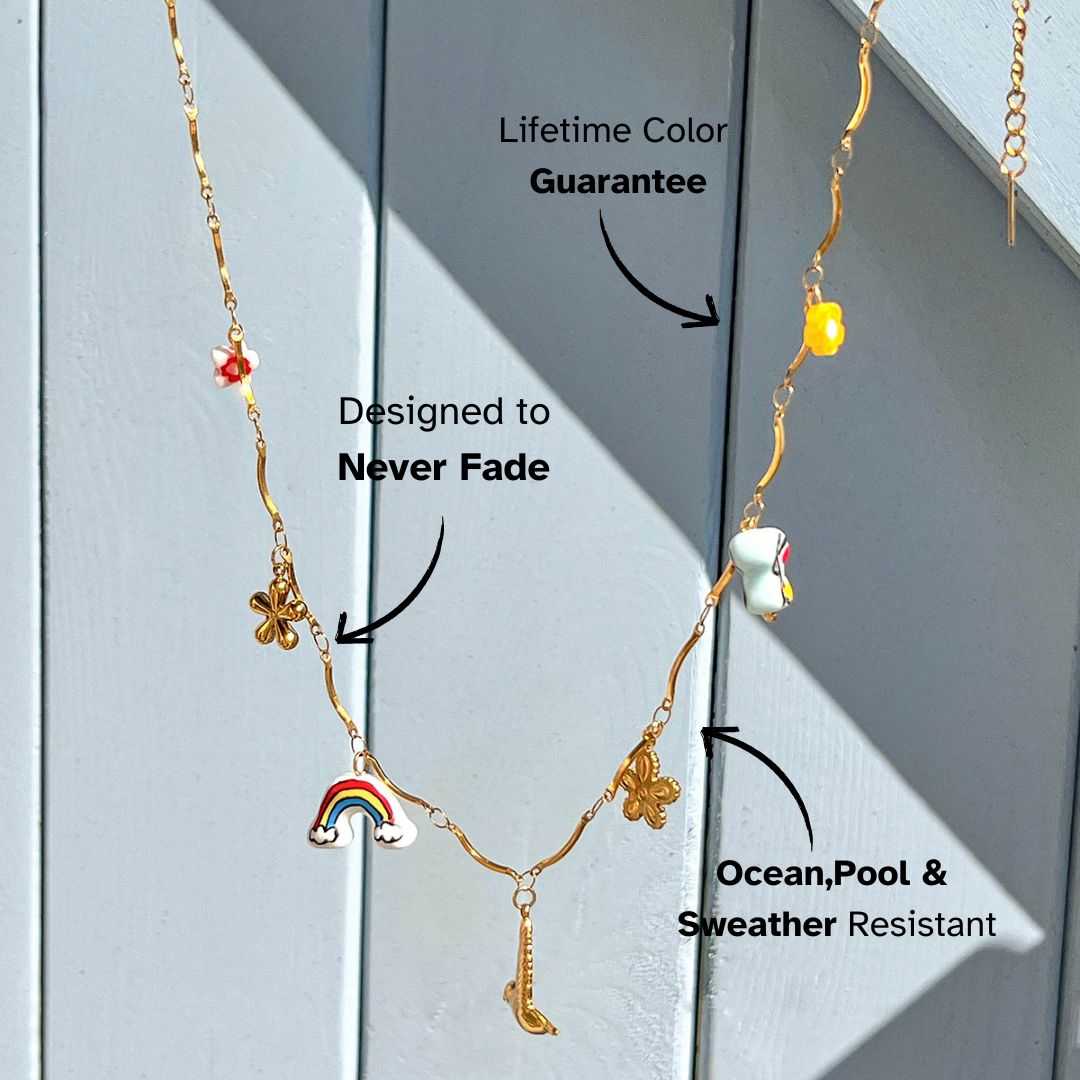 Whimsical gold chain necklace with enamel rainbow, flower and saxophone charms, photographed in sunlight.