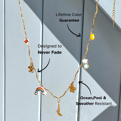 Whimsical gold chain necklace with enamel rainbow, flower and saxophone charms, photographed in sunlight.