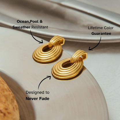Close-up of gold drop-shaped earrings with layered ridges on a dish