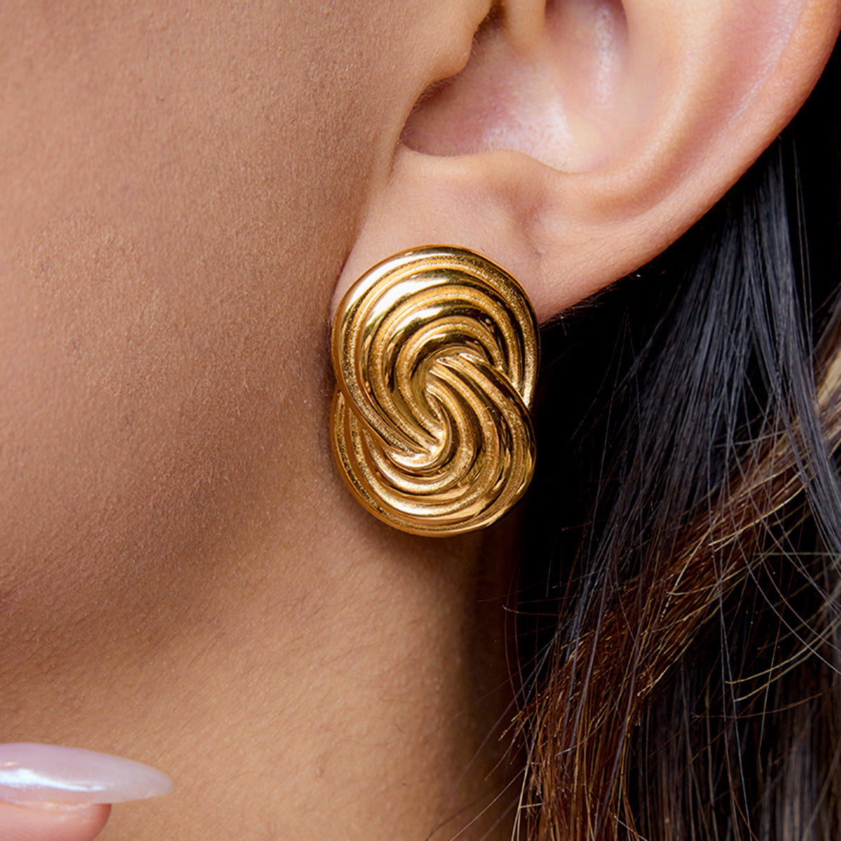 Close-up of bold twisted gold stud earrings on model's ear