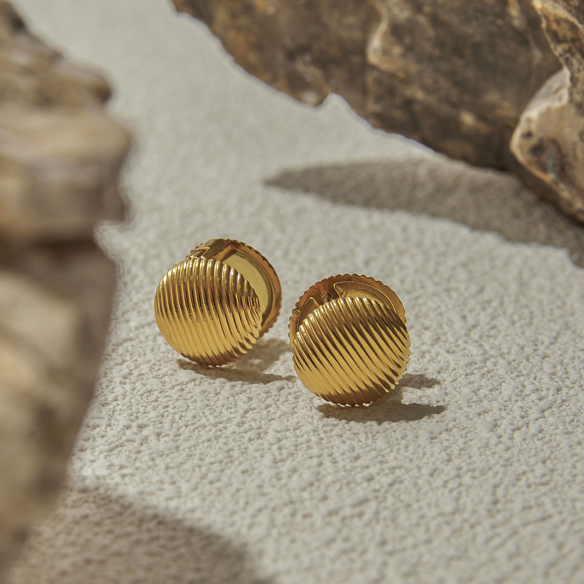 Ribbed gold earrings placed on textured stone surface, elegant outdoor lifestyle setup