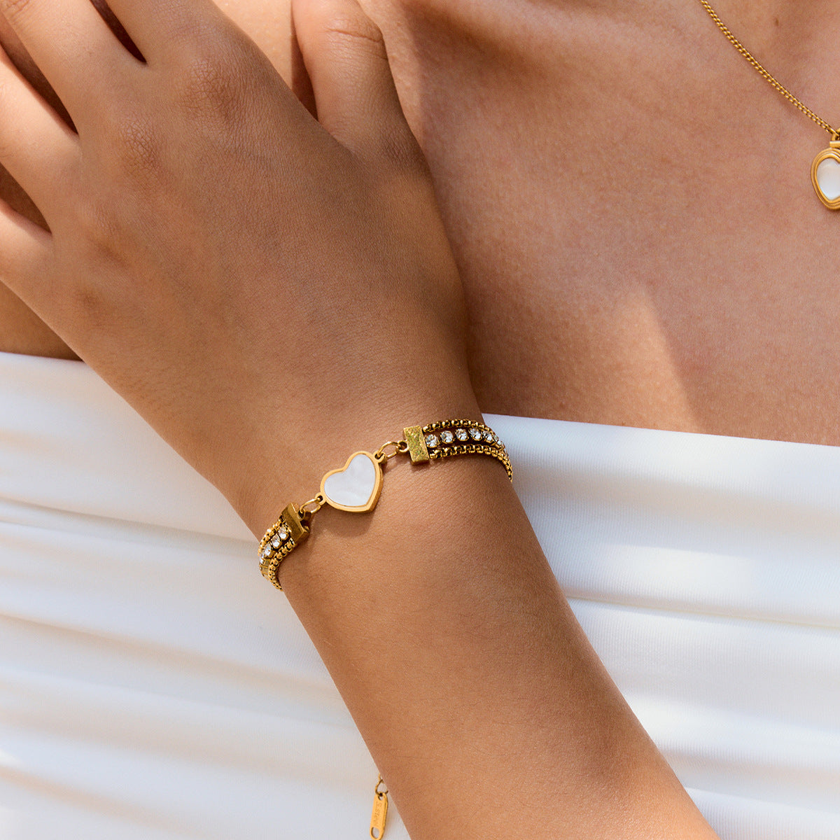 model wearing gold heart bracelet with crystals on wrist in white outfit